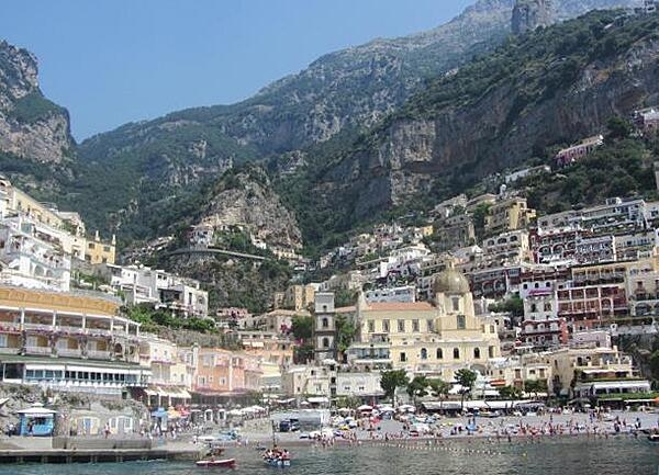 This view show the city of Positano built vertically on the face of a cliff on the rugged Amalfi Coast. In the foreground is the church Our Lady of the Assumption (Santa Maria Assunta) with its gleaming ceramic dome.