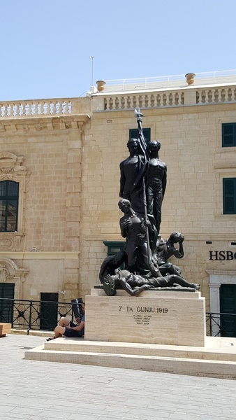 Located in Palace Square, Valletta, the Sette Giugno (Italian for "Seventh of June") Monument commemorates the 1919 uprising against profiteering merchants and the colonial government. This event was a first step towards Maltese independence which arrived in 1964. Sculpted by Anton Agius and inaugurated on 7 June 1986, the monument features six men, two of whom stand defiantly holding the Maltese flag while the other four, representing the victims and the many who were injured in the riots, react to the events - with one succumbing to his wounds. Sette Giugno was made a national holiday in 1989.