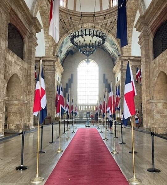 The interior of the Pantheon National in Santo Domingo. Constructed in the 18th century in the Neoclassic-Renaissance style, the building was originally Jesuit church, but later became a warehouse, a theater, and a government building. In 1956, it was renovated as a national mausoleum. A red carpet and national flags, a guard on sentinel duty, and the eternal flame lend reverence to the heroes interred. The light entering through the large glass window in the rear of the building illuminates the solemn interior. A copper chandelier in the center ceiling of the mausoleum reflects light from the building’s dome.