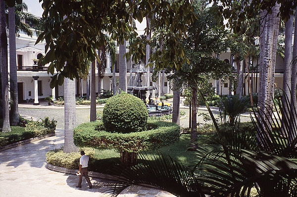 The large courtyard of the Federal Legislative Palace in Caracas is beautifully landscaped with large trees, shrubs, and a fountain.