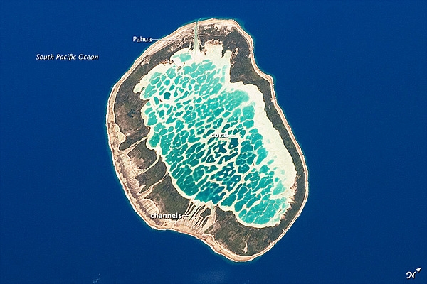 Mataiva Atoll is notable in that its central lagoon includes a network of ridges (white, image center) and small basins formed from eroded coral reefs. Mataiva means “nine eyes” in Tuamotuan, an allusion to nine narrow channels on the south-central portion of the island. The atoll is sparsely populated, with only a single village, Pahua, located on either side of the only pass providing constant connection between the shallow (light blue) water of the lagoon and the deeper (dark blue) adjacent Pacific Ocean. Much of the 10-km (6-mi)-long atoll is covered with forest (greenish brown). Vanilla and copra (dried coconut) are major exports from the atoll, but tourism is becoming a larger part of the economy. Image courtesy of NASA.