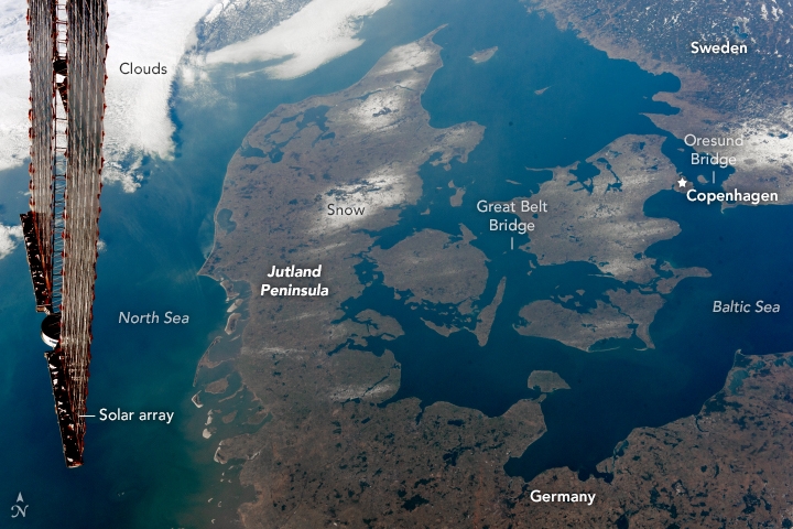 This wintertime photograph taken from the International Space Station shows most of the Kingdom of Denmark, which lies between the North Sea to the west and the Baltic Sea to the east. The winding channels that connect the two seas are international waterways known as the Danish Straits. The long Jutland Peninsula of western Denmark is connected to northern Germany, while the eastern half is comprised mostly of smaller islands in the Danish Archipelago. The larger islands are joined by some of the longest bridges in the World—the Storstrom, the Great Belt, and the Oresund, which joins Denmark to Sweden. The names correspond to the straits between the islands. During the last Ice Age (referred to as the Pleistocene Epoch), much of northwest Europe was covered with thick glaciers. Glacial deposits and kettle lakes were left behind when the ice retreated. Lowland areas now dominate Denmark, which has a mean elevation of just 34 m (118 ft) above mean sea level. Image courtesy of NASA.