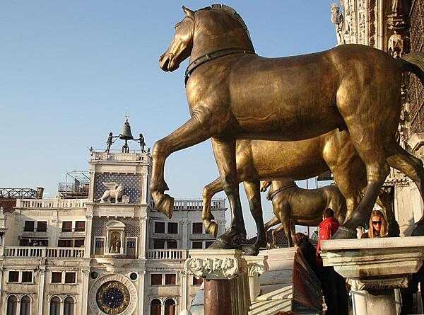 View of St. Mark's Square in Venice, Italy, showing the famous Greek horses and the astronomical clock. The bronze horses were originally installed at the Hippodrome in Constantinople and date back to at least the 4th century. In 1254, they came to Venice, where they remained until Napoleon took them to Paris in 1797. In 1815, the horses were returned to Venice, and the originals are now in St. Mark's Museum. The original astronomical clock was built between 1496-99.