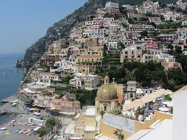View of the city of Positano on the rugged Amalfi Coast showing the church Our Lady of the Assumption in the foreground and homes built vertically on a cliff in the background.