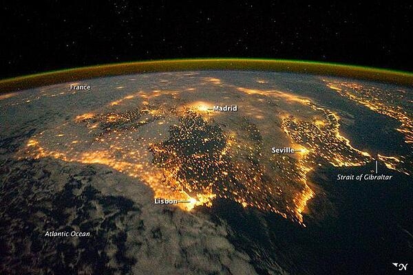 The city lights of Spain and Portugal define the Iberian Peninsula in this photograph taken from the International Space Station (ISS) on 4 December 2011. Several large metropolitan areas are visible, marked by their relatively large and brightly lit areas, such as the capital cities of Madrid, Spain - located near the center of the peninsula&apos;s interior - and Lisbon, Portugal - located along the southwestern coastline. The ancient city of Seville, visible at image right to the north of the approximately 14 km (9 mi)-wide Strait of Gibraltar, is one of the largest cities in Spain. The view is looking outwards from the ISS towards the east.

The network of smaller cities and towns in the interior and along the coastline attest to the areal extent of human presence on the Iberian landscape. Blurring of the city lights is caused by thin cloud cover (image left and center), while the cloud tops are dimly illuminated by moonlight. Though obscured, the lights of France are visible near the horizon line at image upper left, while the lights of northern Africa are more clearly discernable at image right. The gold to green line of airglow, caused by excitation of upper atmosphere gas molecules by ultraviolet radiation, parallels the horizon line (or Earth limb). Image courtesy of NASA.
