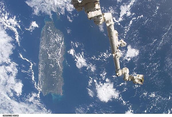 The Space Station Remote Manipulator System (SSRMS) or Canadarm2 appears against the Caribbean Sea in this view taken from the International Space Station. Puerto Rico is the large island on the left side of the frame. Image courtesy of NASA.