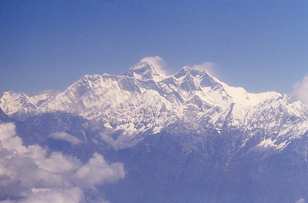 An aerial view of the Himalayas with windswept Mount Everest in the center. The mountain is located on the Nepal-China border and is shared by both countries. Mount Everest is the highest point on Earth above sea level at 8,849 m (29,025 ft). The mountain was named after Sir George Everest, a British surveyor and geographer who served as the Surveyor General of India from 1830-1843.