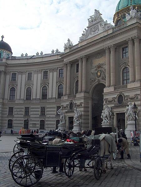 Horse-drawn coaches (known as fiaker in Vienna) await riders in front of the grand Michaelertrakt (Michael&apos;s Wing) of the Hofburg (Imperial Palace).