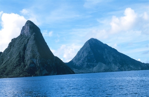The distinctive Twin Pitons, seen here from the sea, are the national symbol of Saint Lucia. The Pitons are two mountainous volcanic plugs (created when magma hardens within a vent on an active volcano).  Gros Piton is 798 m (2,619 ft) high and Petit Piton is 743 m (2,438 ft) high; both are located near the town of Soufriere, Saint Lucia. The Twin Pitons were designated a UNESCO World Heritage site in 2004.
Photo courtesy of NOAA / Anthony R. Picciolo.