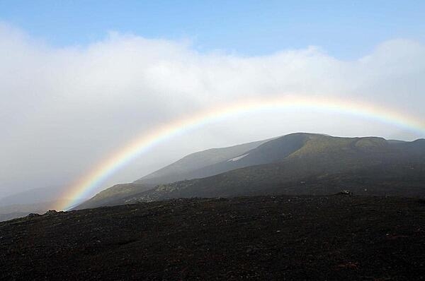 A rainbow envelopes the peak of Hekla volcano, a stratovolcano located in southern Iceland. It is one of the island's most active volcanoes, having erupted more than 20 times since the ninth century A.D. Hekla is 1,491 m (4,892 ft) high and its name is Icelandic for “short hooded cloak,” which probably refers to the clouds that frequently hang over its summit. However, in the Middle Ages, the Norse called it the "Gateway to Hell." The volcano is responsible for the creation of more than 10% of the landmass of Iceland over the last 1000 years. Iceland is situated on top of a seismic hotspot, subjecting it to earthquakes and severe volcanic activity.