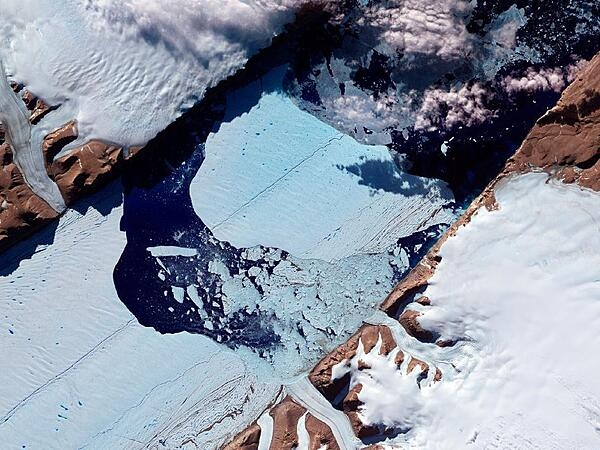 The Petermann Glacier grinds and slides toward the sea along the northwestern coast of Greenland, terminating in a giant floating ice tongue. Like other glaciers that end in the ocean, Petermann periodically calves icebergs. In July 2012, a massive ice island broke free and gradually drifted down the fjord, away from the floating ice tongue from which it calved. This satellite image has been rotated and north is toward the right. Analysis of the  image reveals that the iceberg covers an area of about 32.3 sq km (12.5 sq mi). Image courtesy of NASA.