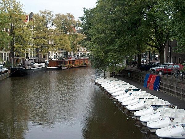 Lined up tourist boats on an Amsterdam canal resemble a row of shoes. The floating Tulip Museum is in the background.
