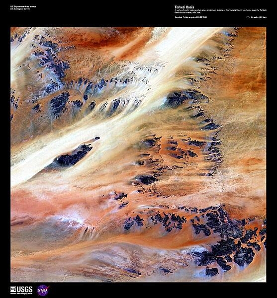 Only 10,000 years ago grasses covered the Sahara Desert and mammals such as lions and elephants roamed the land. Now only two percent of the Sahara hosts oases, patches of land usually centered on natural water springs where crops will grow and where nearly two million people live. In this enhanced satellite image, a series of dark rocky outcroppings contrast with colorful windblown rivers of sand near the Terkezi Oasis in Chad. Image courtesy of USGS.