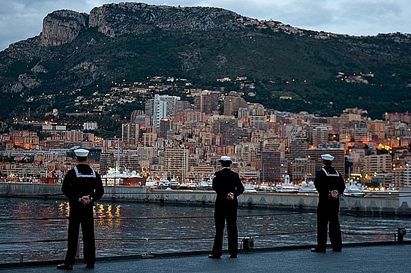 Sailors stationed aboard the amphibious command ship USS Mount Whitney man the rails as the ship arrives in Monaco for a port visit to participate in Monaco's National Day celebration in 2008. Much of Monaco is visible in the background and consists of the built-up area along the coast. Photo courtesy of the US Navy/ Petty Officer 2nd Class Brian Glunt.